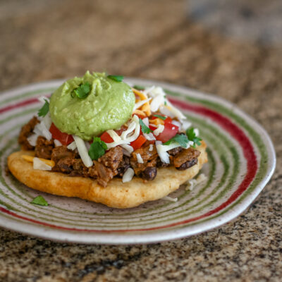 A taco salad on fry bread with a guacamole and cilantro topping.