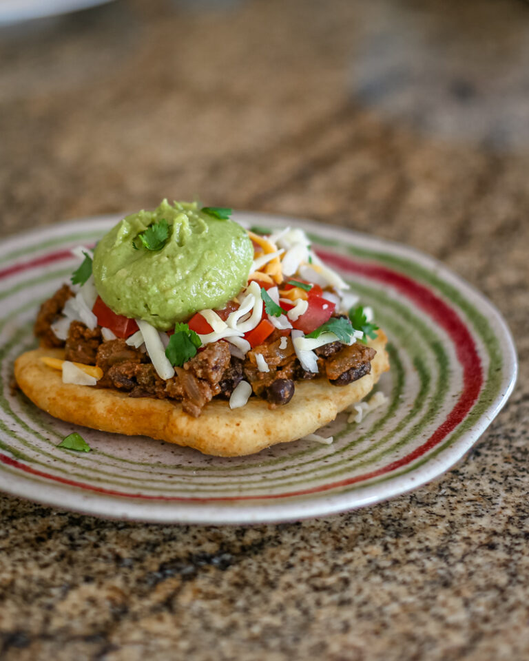 A taco salad on fry bread with a guacamole and cilantro topping.