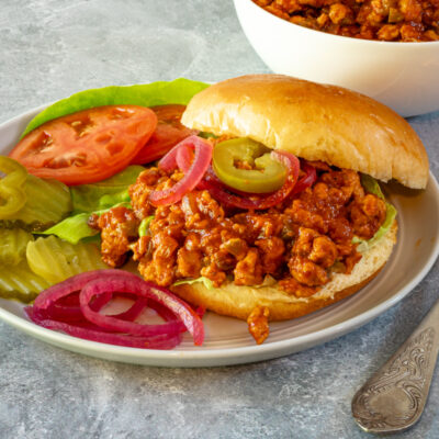 A plate with a turkey sloppy joe with tomatoes and pickles.