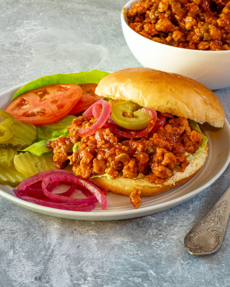 A plate with a turkey sloppy joe with tomatoes and pickles.