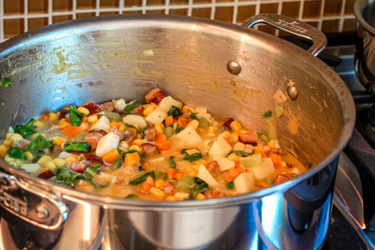 Adding potatoes and spinach to the sausage and vegetable chowder mixture.