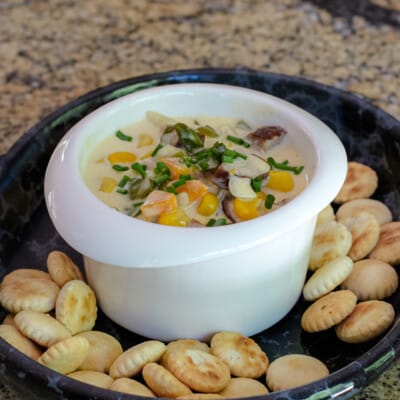 Creamy vegetable and sausage chowder shown in a bowl with chives for garnish and oyster crackers.
