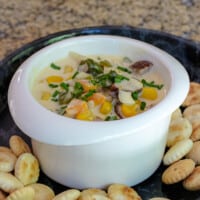 Creamy chowder with vegetables and diced smoked sausage in a small bowl with crackers surrounding it.