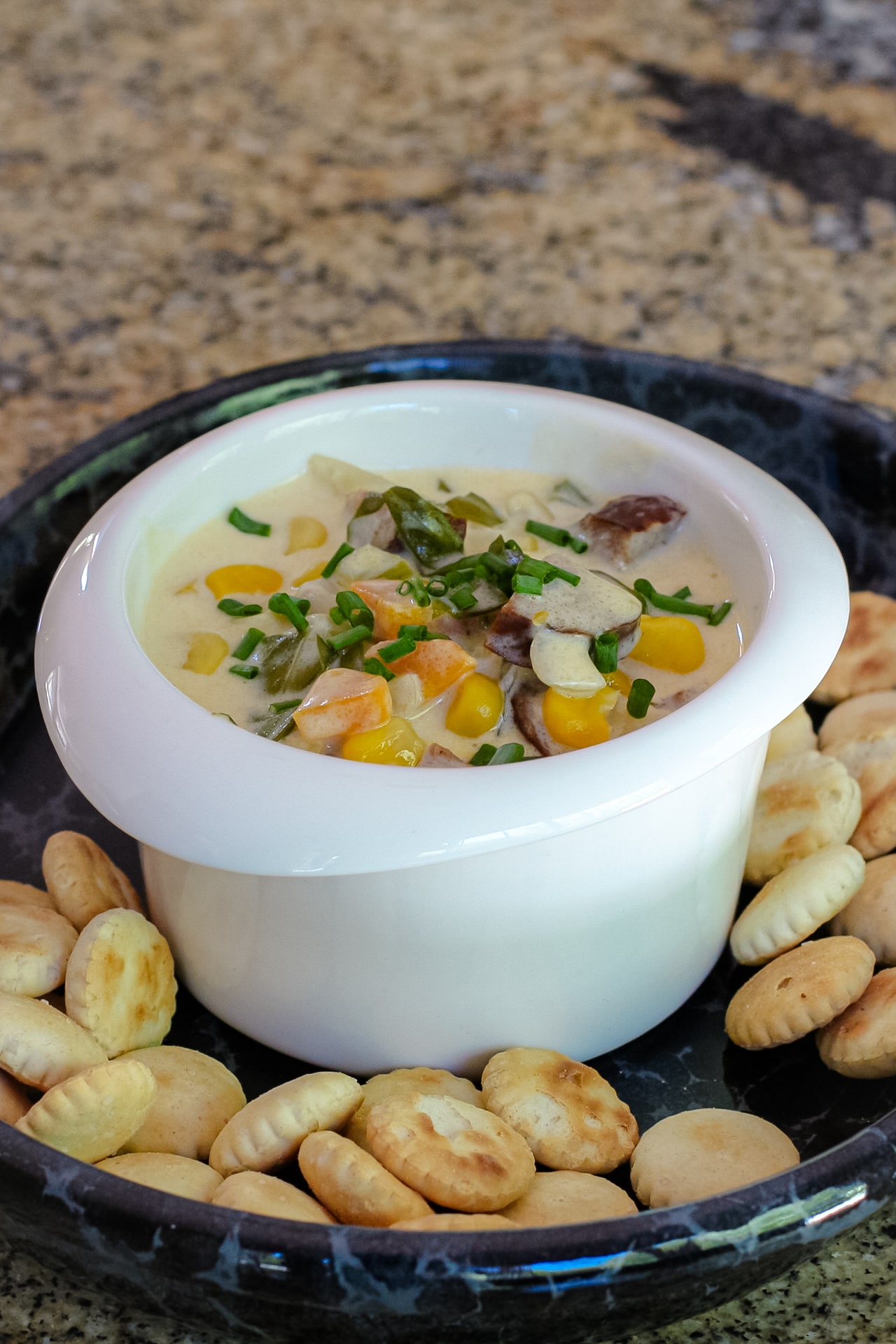Creamy chowder with vegetables and diced smoked sausage in a small bowl with crackers surrounding it.