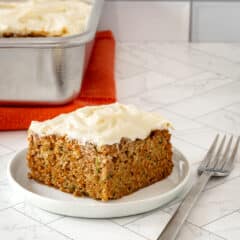 A zucchini carrot cake slice on a white plate with cream cheese frosting.