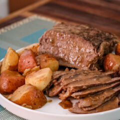 Roast beef with potatoes and carrots on a white plate.