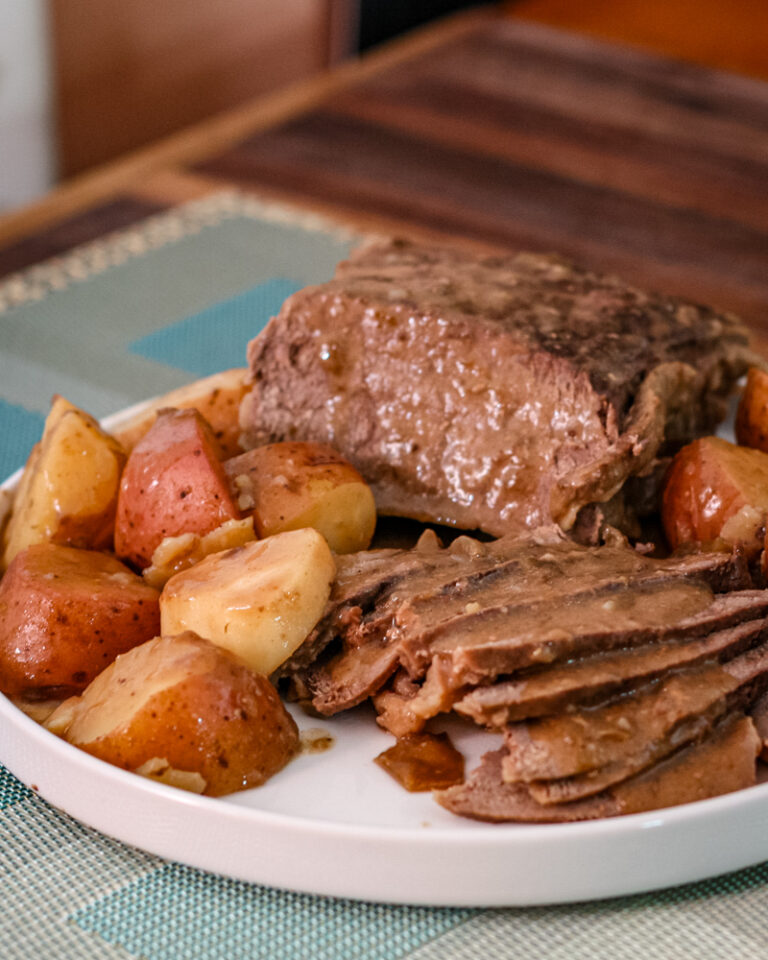 Roast beef with potatoes and carrots on a white plate.