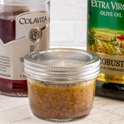 Freshly prepared seasoned meat mixture in a glass jar with olive oil and canned tomatoes in the background.