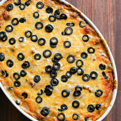 Overhead photo of a beef enchilada casserole with a topping of cheese and black olives.