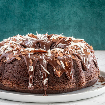 Moist chocolate bundt cake on a plate, decorated with a chocolate glaze and chocolate shards.
