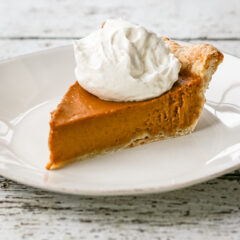 A bourbon pumpkin pie on a white plate with whipped cream topping.
