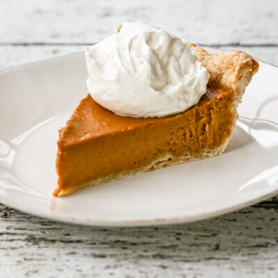 A bourbon pumpkin pie on a white plate with whipped cream topping.