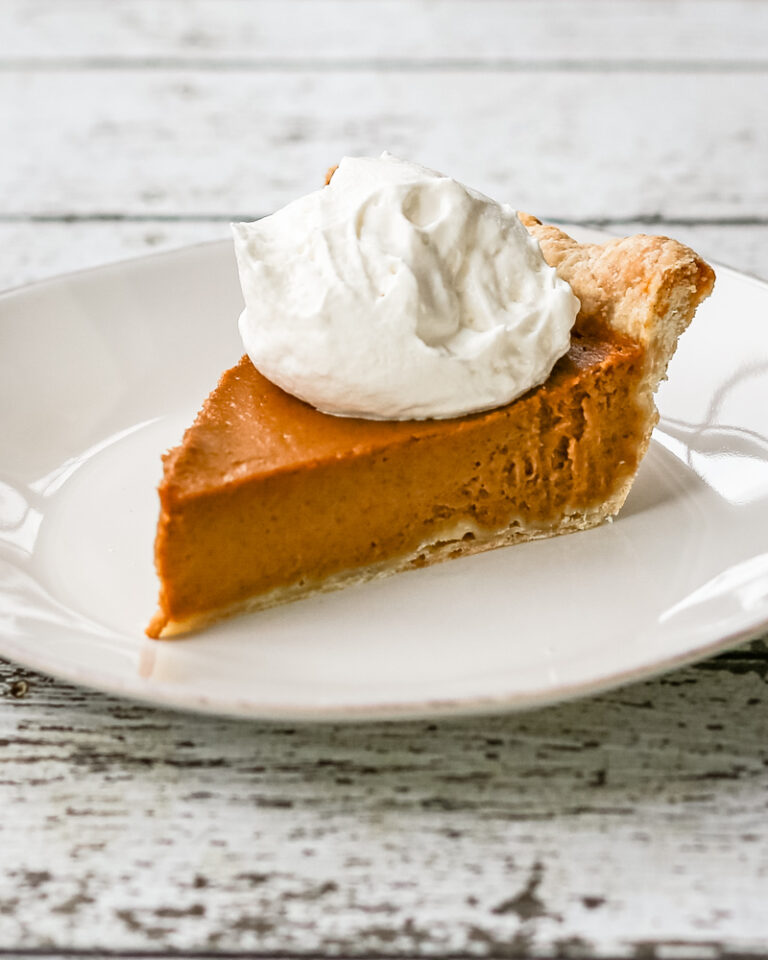 A bourbon pumpkin pie on a white plate with whipped cream topping.