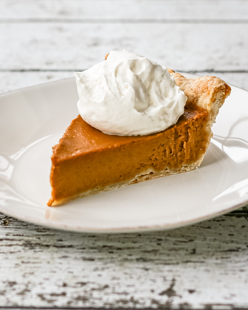 A bourbon pumpkin pie on a white plate with whipped cream topping.