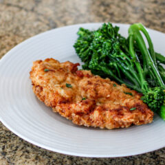 fried chicken breast cutlets on a plate with broccolini