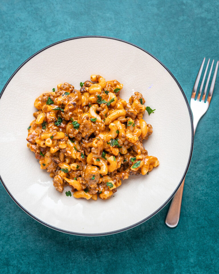A serving of cheeseburger mac on a light colored plate with a fork, garnished with parsley.