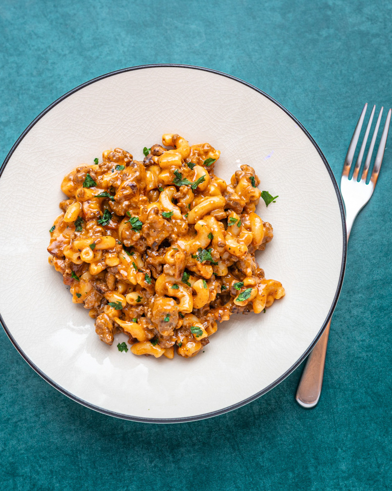 A serving of cheeseburger mac on a light colored plate with a fork, garnished with parsley.