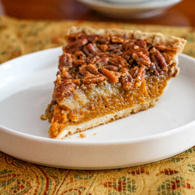 A slice of pumpkin pecan pie on a white plate.
