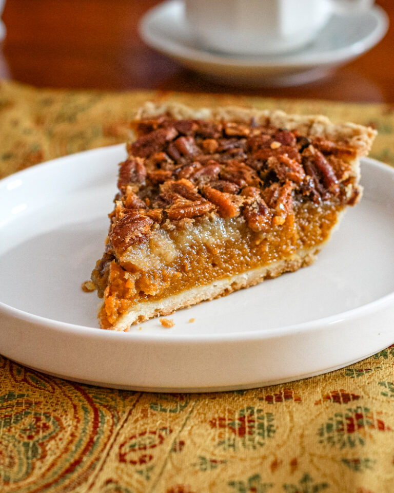 A slice of pumpkin pecan pie on a white plate.