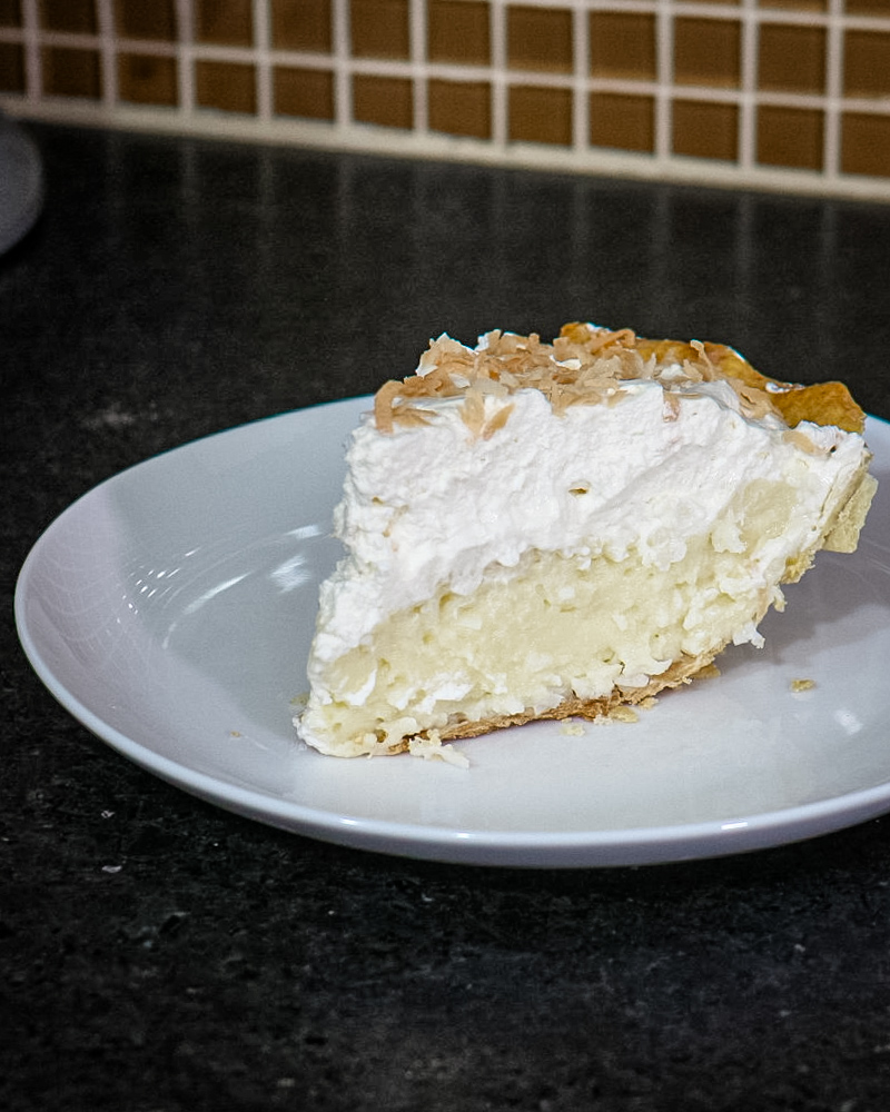 A slice of coconut cream pie with toasted coconut garnish