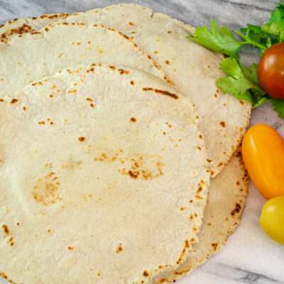 A stack of homemade corn tortillas with some cilantro and grape tomatoes, on a marble surface.