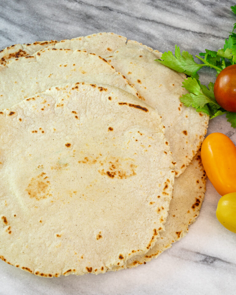 A stack of homemade corn tortillas with some cilantro and grape tomatoes, on a marble surface.