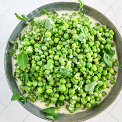 creamed peas in a serving bowl with pea shoots