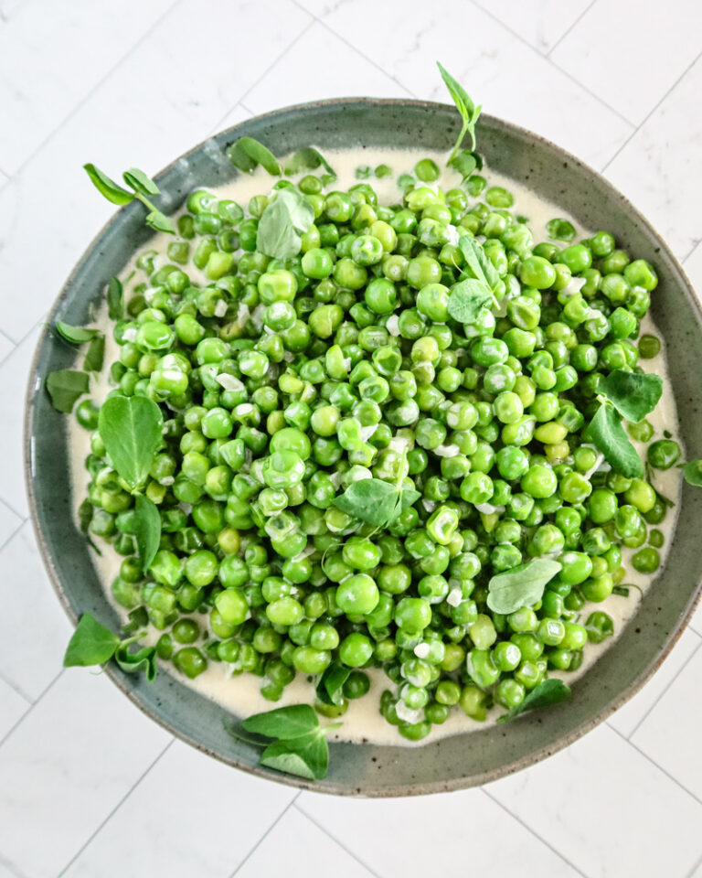 creamed peas in a serving bowl with pea shoots