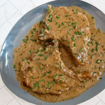 Apple cider pork chops with chives, on a large blue platter.