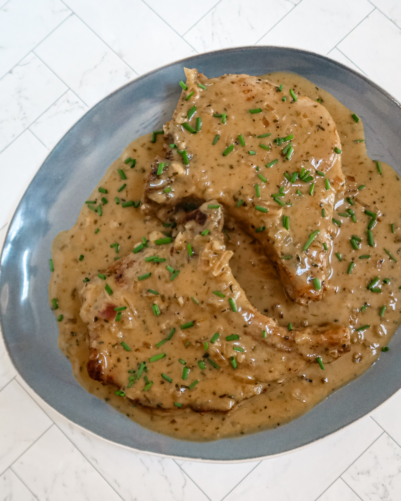 Apple cider pork chops with chives, on a large blue platter.