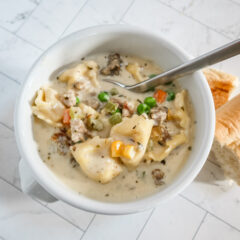 A bowl of sausage and tortellini soup with bread on the side.