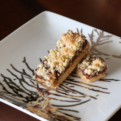 Date bars with shortbread crust and crumb topping on a decorative square plate.