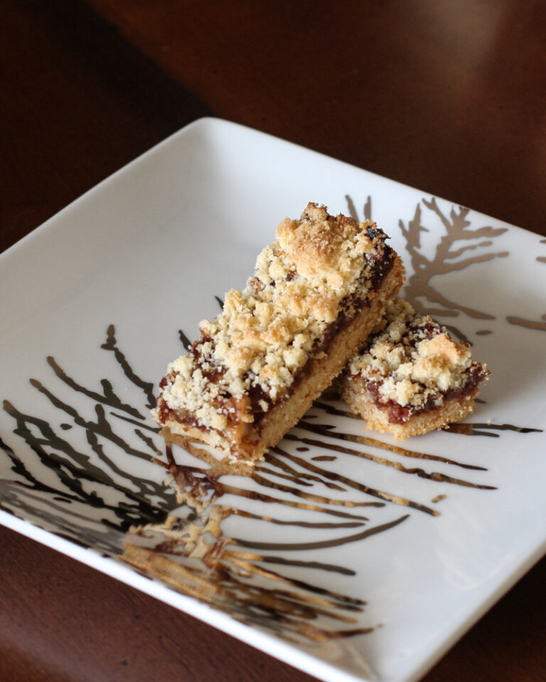 Date bars with shortbread crust and crumb topping on a decorative square plate.