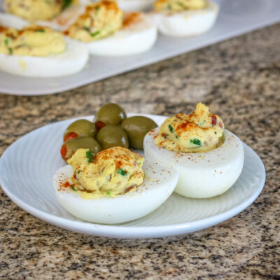 deviled eggs with bacon on a plate with more in the background