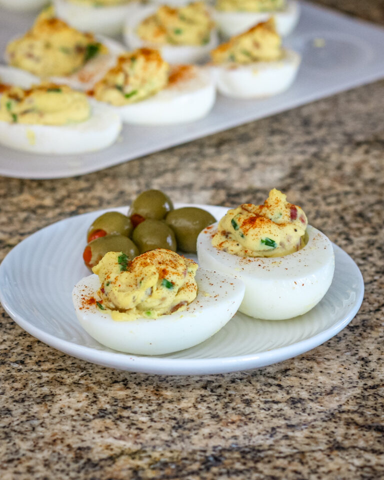 deviled eggs with bacon on a plate with more in the background