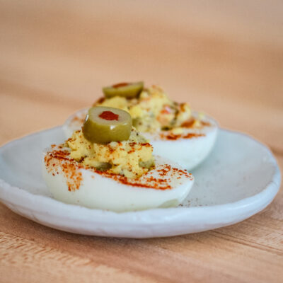 deviled eggs with olives on a white snack plate.