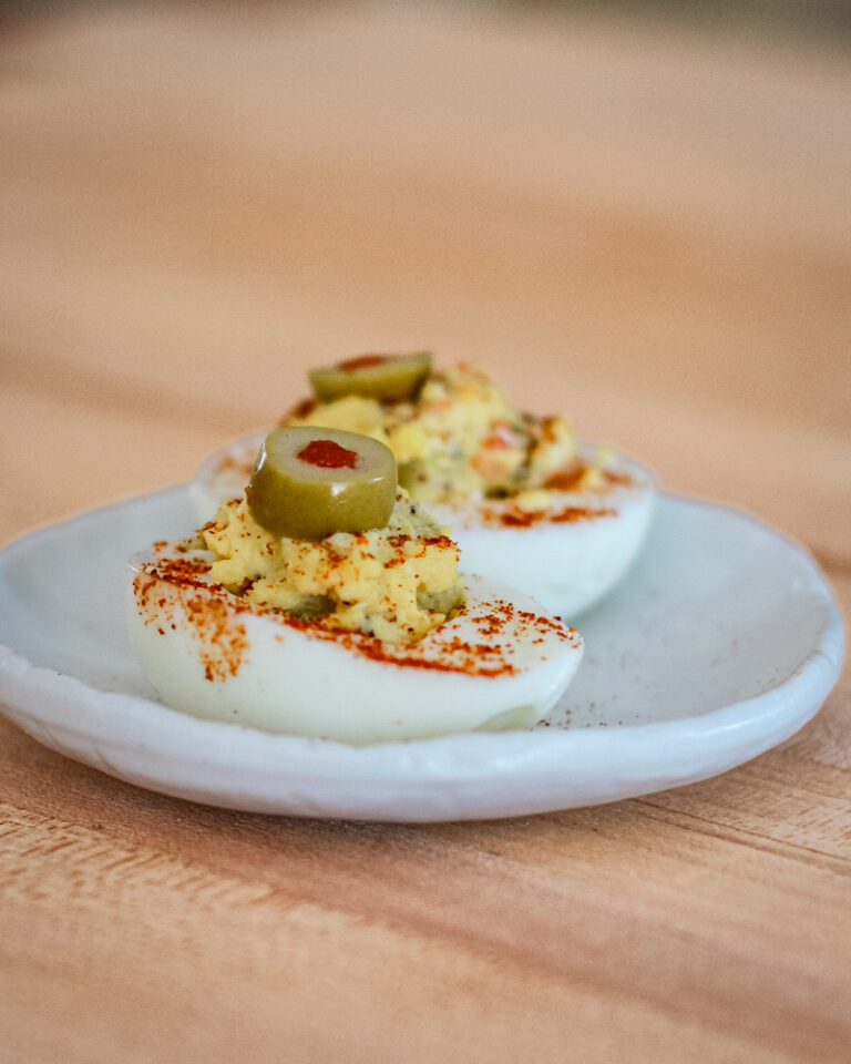 deviled eggs with olives on a white snack plate.