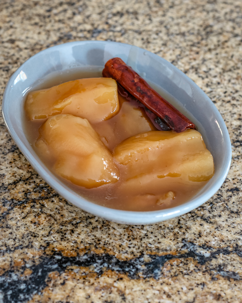 slow cooked apples in a small dish with a cinnamon stick