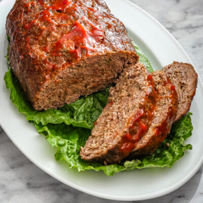 slices of meatloaf on a platter lined with lettuce leaves.