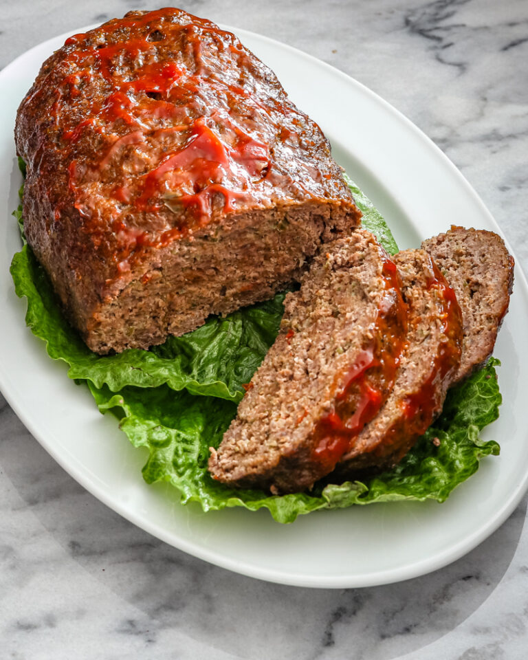 slices of meatloaf on a platter lined with lettuce leaves.
