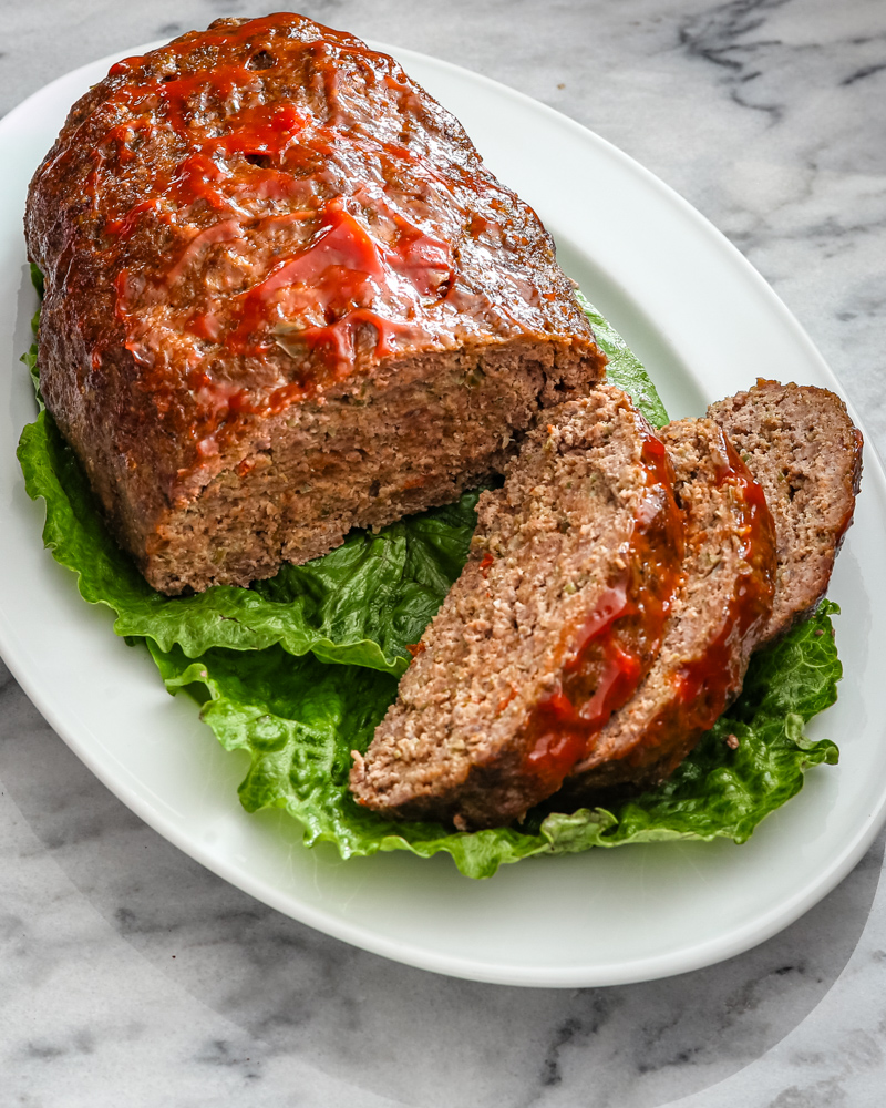 slices of meatloaf on a platter lined with lettuce leaves.