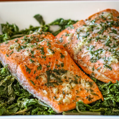 garlic and herb salmon on a bed of spinach in a white dish.