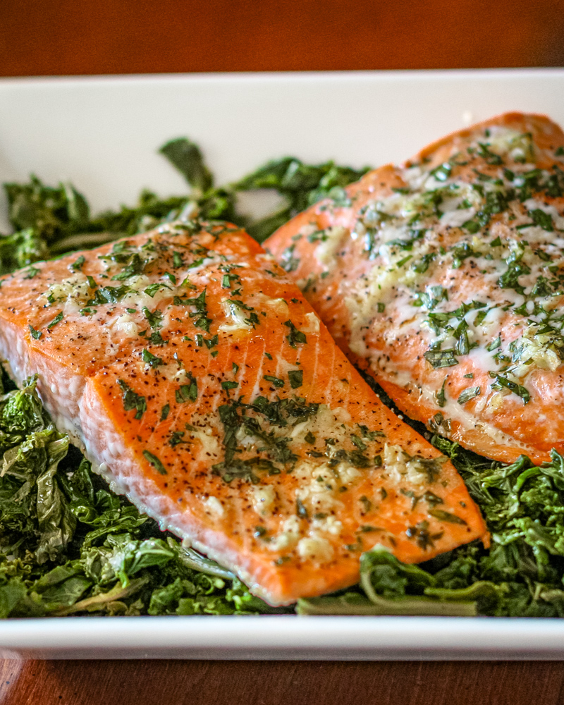 garlic and herb salmon on a bed of spinach in a white dish.