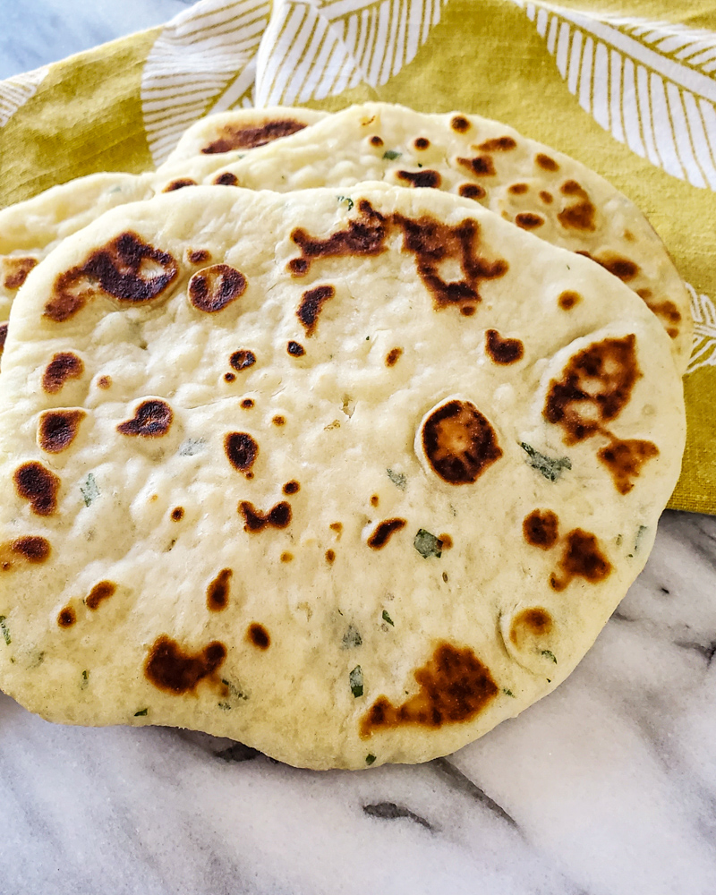 Homemade garlic naan on a yellow towel.