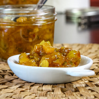 Green tomato chutney in a small plate with the canning jar and spoon in the background.