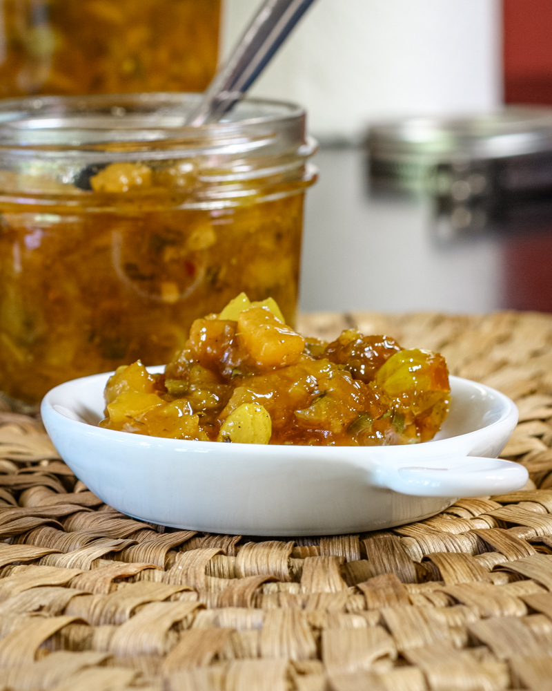 Green tomato chutney in a small plate with the canning jar and spoon in the background.