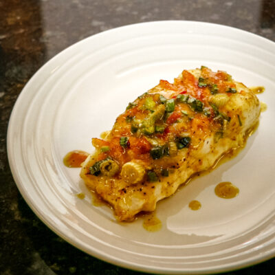 Halibut with a green onion and curry topping on a white plate.