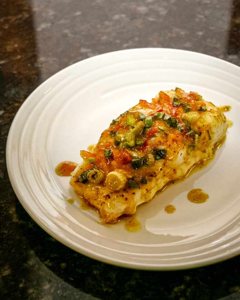 Halibut with a green onion and curry topping on a white plate.