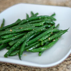 Freshly cooked green beans with garlic and seasoning on a white plate.