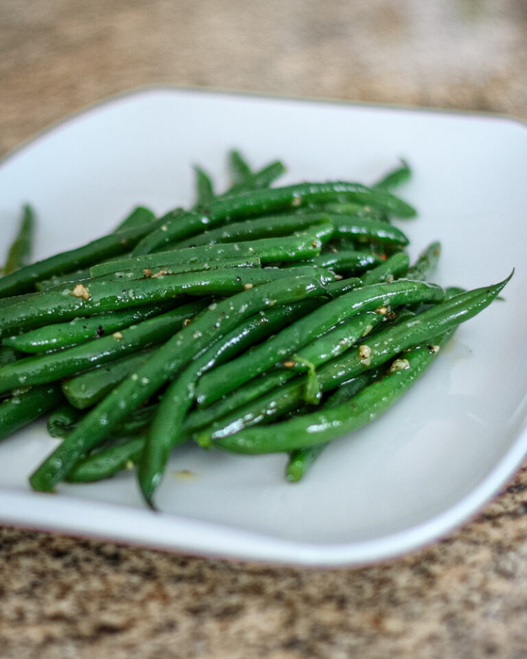 Freshly cooked green beans with garlic and seasoning on a white plate.